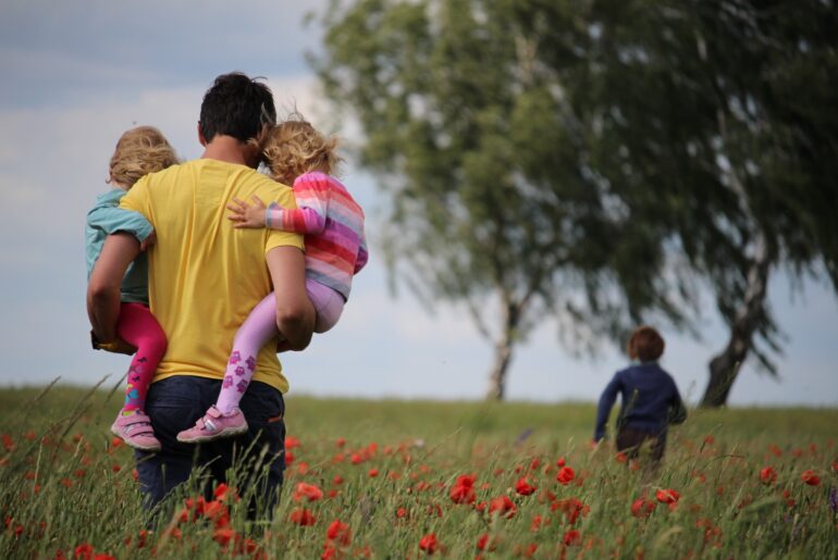 a father carries two of his children in a field
