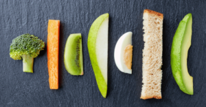 in bite sized pieces, a slice of broccoli, carrot, kiwi, pear, egg, bread and avocado are lined up next to one another in a perfect example of what's appropriate for baby-led weaning. 